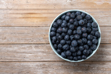 Blueberries in green bowl on wooden table. Top view. Copy space