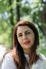 Naklejka premium Portrait of a pretty 45 year old woman with red lips looking at camera happy and confident, sunny day in nature. Concept of maturity, happiness and lifestyle