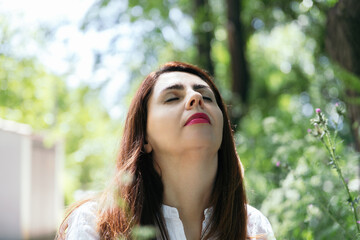 Naklejka premium Portrait of a pretty 45 years old woman with closed eyes and face upwards enjoying the sun and nature. Concept of maturity, happiness and wellness