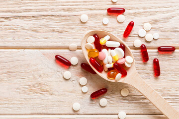 Vitamin capsules in a spoon on a colored background. Pills served as a healthy meal. Red soft gel...