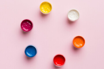 jars with gouache of different colors on Colored background. hobby painting. Top view with empty...