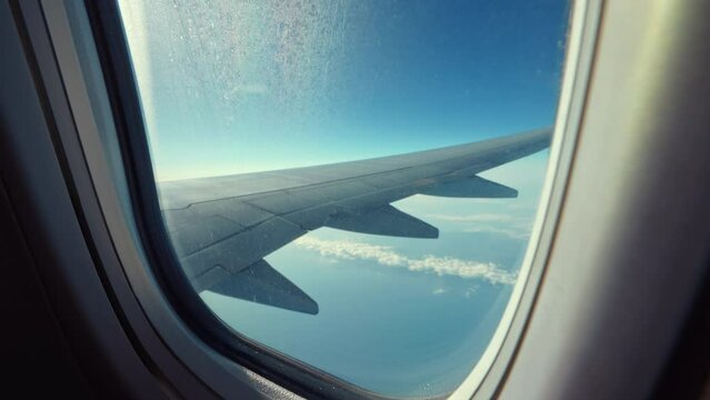 Aerial view from airplane from porthole window of passenger flight of aircraft in summer on sunny day.  Earth landscape and clouds through window. Travel concept. Tourism. Go Everywhere