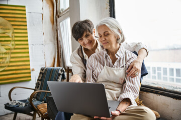 Two women interact with laptop screen in cozy setting.