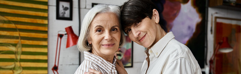 A mature lesbian couple standing together in an art studio.