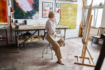 Woman sits on a chair in front of an easel, deep in thought and contemplation.