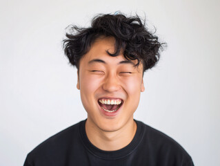 Happy Young Asian Man with Curly Hair Laughing, Displaying Positive Emotion in Casual Black Shirt