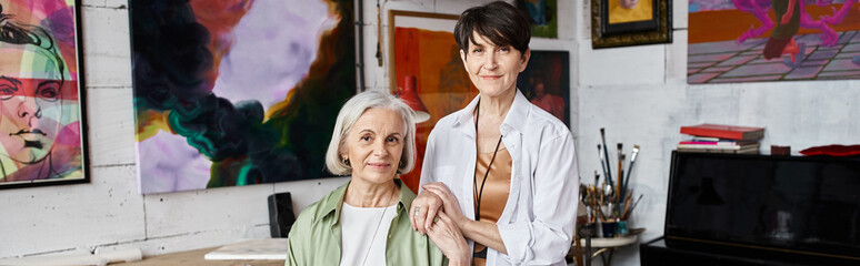 Two woman standing in front of paintings in an art studio.