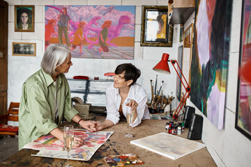 Two woman discussing artwork at table in studio.