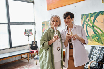 A mature lesbian couple in an art studio, standing close together.