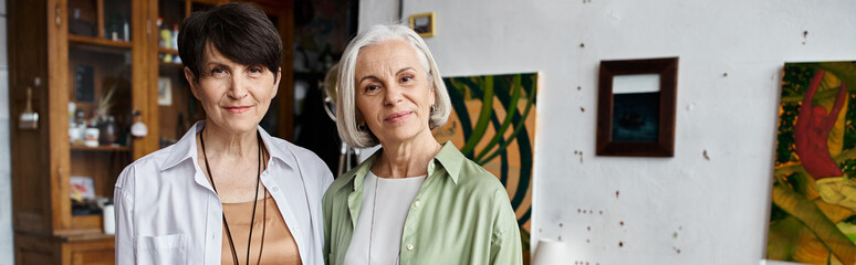 Mature lesbian couple in art studio, standing side by side.