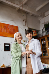 Two mature women, standing in an art studio, exude a sense of togetherness.