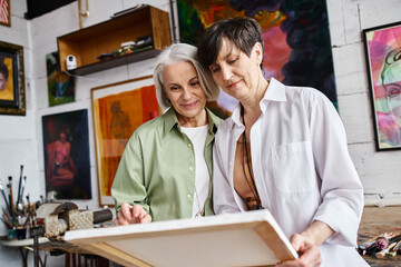 A mature lesbian couple admire artwork together in a studio.