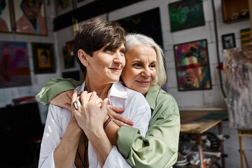 Two women tenderly embrace in an art studio.