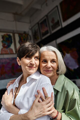 Two mature women hugging in an art studio.