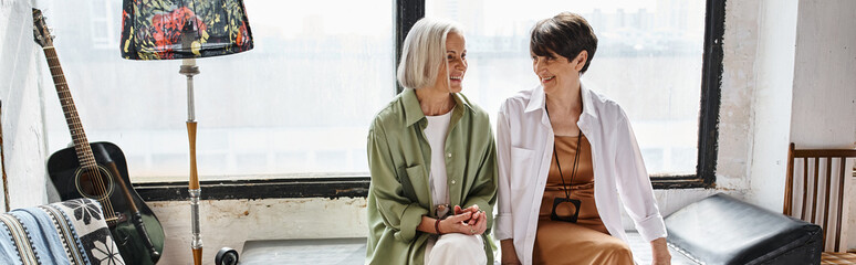Two mature women standing close, embracing each other in an art studio.