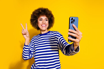 Photo of nice young girl take selfie show v-sign wear striped shirt isolated on yellow color...
