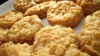 Chicken nuggets made by cutting or grinding chicken, mixed with seasonings, fillers, and binders, shaped, coated, and fried until golden brown. Junk food concept. Fast-food background. 
