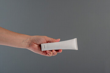 Plastic white tube for cream or lotion. Skin care or sunscreen cosmetic with hand on grey background.