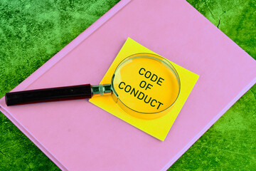 Business concept text. The words CODE OF CONDUCT through a magnifying glass on a yellow sticker...