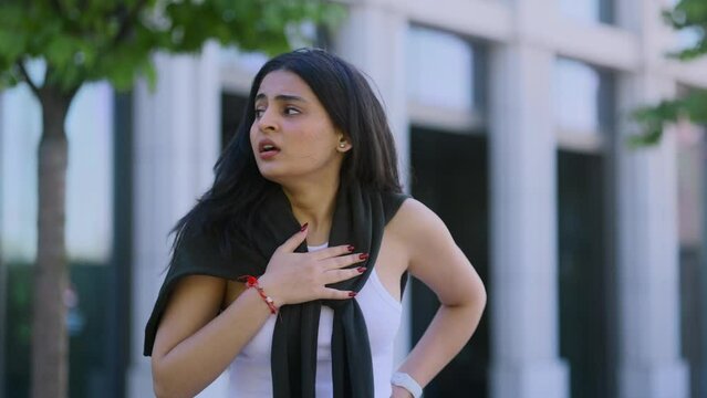 Worried young indian woman walking down the urban street while has panic heart attack hold hand on chest and try to calm down alone Anxious female with mental health problem outdoors