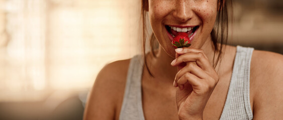 Happy, woman and eating strawberry in kitchen for nutrition, health and wellness in home. Female...