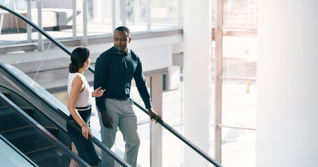Business people, escalator and discussion with colleague for work trip, travel or career opportunity at office. Businessman and woman talking on electric staircase or lift in immigration at workplace