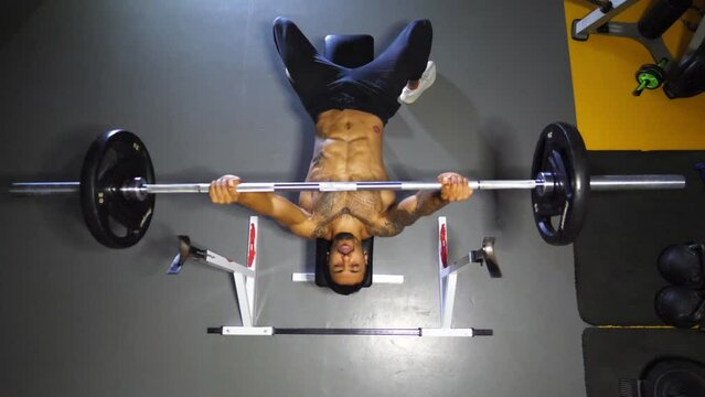 Strong black sportsman doing bench press workout with a barbell at sport club. Muscular athlete doing weightlifting exercises at modern gym. Healthy and active lifestyle concept. Top view