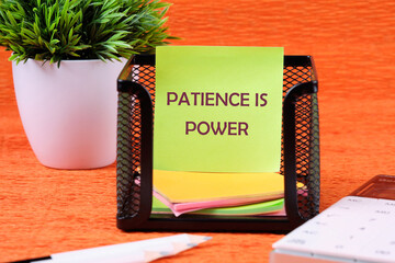 Personal development concept. Words PATIENCE IS POWER on a sticker on a stand near a calculator, pencils and a green plant in the background