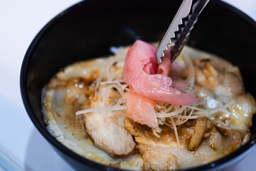 Donburi rice topped with chashu pork slices topped with pink pickled ginger in a black bowl.