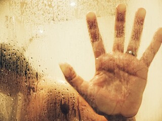 woman taking a shower with hand on glass wall