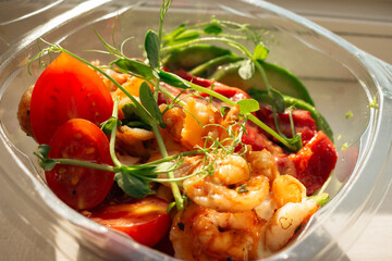 Grilled shrimps, red bell pepper with avocado and tomato in plastic bowl. Poke bowl in sunlight. Traditional asian food. Street food to go. Healthy eating concept. Seafood poke bowl with pea sprouts.