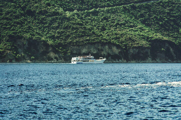 Small car and passengers ferry sailing next to a green plantation coastline in Lefkada Ionian Island Greece.