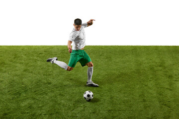 Side view photo of soccer player kicking, passing ball in motion on green grass field against a...