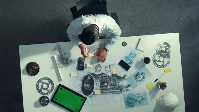 Top down view of skilled engineer writing and planning turbine engine design while sitting at meeting table with gear and electronic generator scatter around. Technician taking a note. Alimentation.