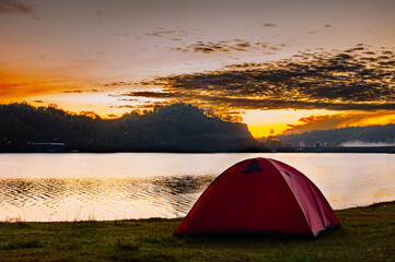 A red tent stands on the edge of the lake with the setting sun appearing at the end of the lake