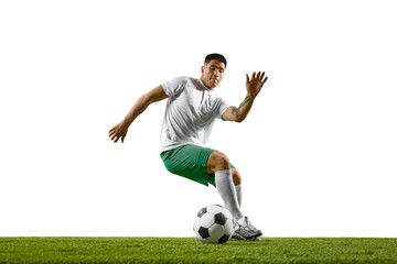 Young athletic man training dribbling technique in motion on green lash field against white studio...