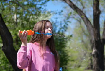 Charming girl blowing soap bubbles in sunny park in summer. Concept of happiness, fun and childhood. Selective focus.