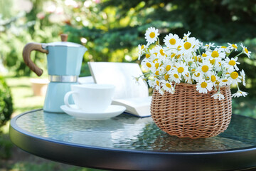 Bouquet of flowers in basket with book, cup and coffee pot. Bouquet of chamomile flowers. Spring, summer holidays, Easter, mother's day. Side view. Space for text.