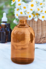 Bottle of essential oil with chamomile flowers. Side view. Space for text.       