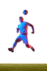 Soccer player jumps leaping prepares to head soccer ball, with his body twisted in motion on field in neon light against white studio background. Concept of sport, competition, tournament, movement