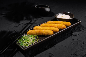 Gourmet breaded fish sticks on elegant black plate