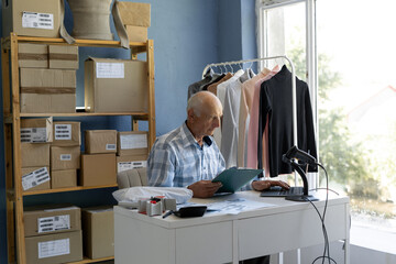 An elderly business man, an online store manager, uses laptop to monitor sales, check statistics,...