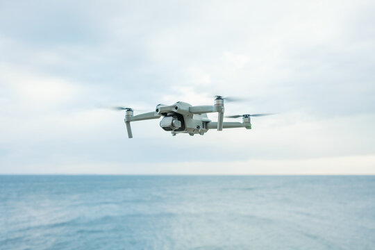 A micro drone hovers in the air above a water horizon