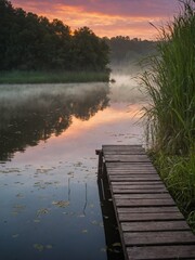 Obraz premium Wooden pier reaches out into tranquil lake, with misty veil hovering above waters surface. Scene bathed in warm hues of sunrise, sunset, reflected in still water.