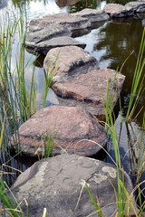 Small stony footbridge, stone bridge over the stream or little pond. Pathway through the stream