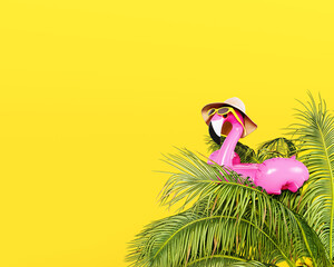 Pink flamingo with hat and sunglasses on palm tree. Summer travel concept design on yellow...