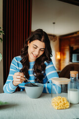 One young caucasian woman is eating corn flex breakfast at home before work	
