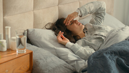 Unhappy woman lying on bed holding head bedroom home girl female headache ill migraine sick rubbing...