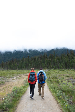 Two people walk away wearing backpacks on a dirt trail.