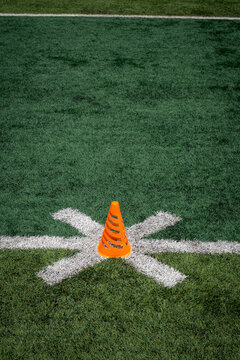 An orange athletic cone on a turf football field.
